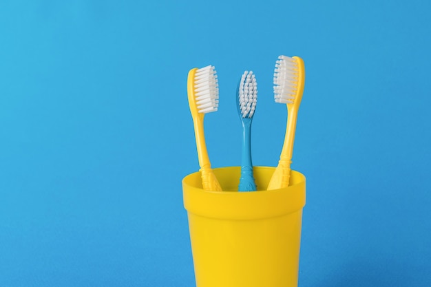 Duas escovas de dentes amarelas e uma azul em um copo amarelo em um fundo azul O conceito de cuidados bucais