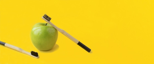 Duas escovas de dentes de bambu e maçã verde no fundo amarelo Copiar espaço