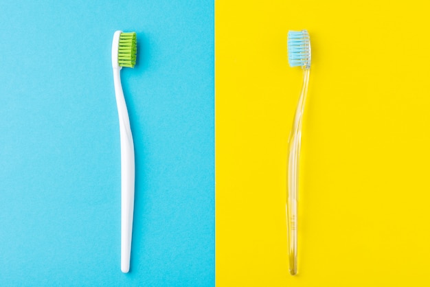 Duas escovas de dentes de plástico sobre um fundo azul e amarelo pastel, estilo liso leigo