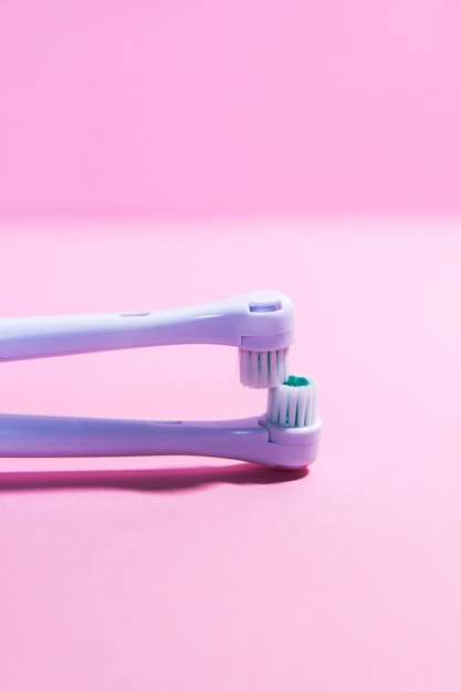 Duas escovas de dentes elétricas em um fundo rosa claro suave.