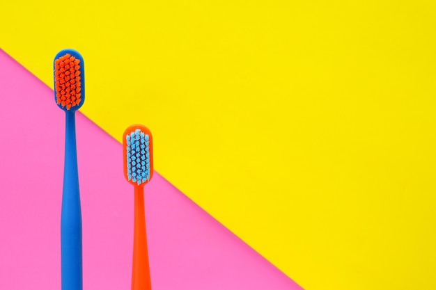 Duas escovas de dentes multicoloridas em uma cópia de fundo amarelo-rosa spacexA