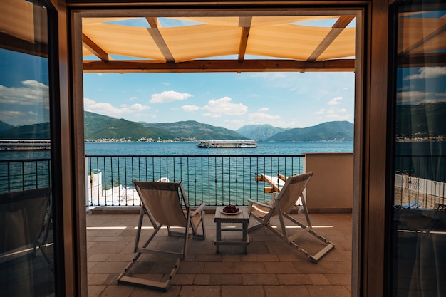 Duas espreguiçadeiras na varanda do quarto do hotel com vista para o mar e um barco turístico de passagem