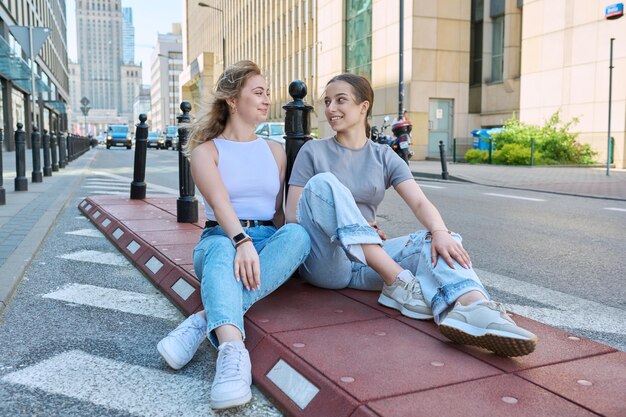 Duas estudantes rindo olhando para a câmera edifícios de estrada de estilo urbano moderno no fundo