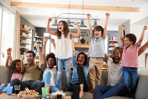 Foto duas famílias assistindo esportes na televisão e torcendo