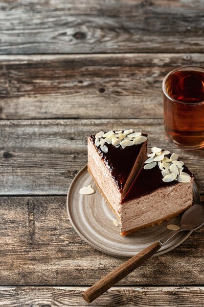 Duas fatias de cheesecake de chocolate com cobertura de pétalas de amêndoa e xícara de chá em fundo de madeira com espaço de texto