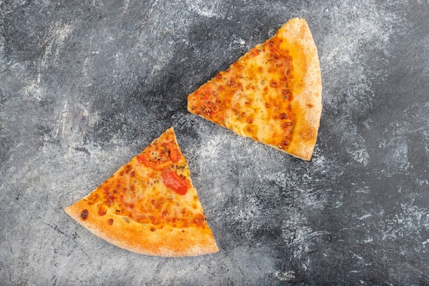 Duas fatias de deliciosa pizza de queijo colocadas sobre fundo de pedra.