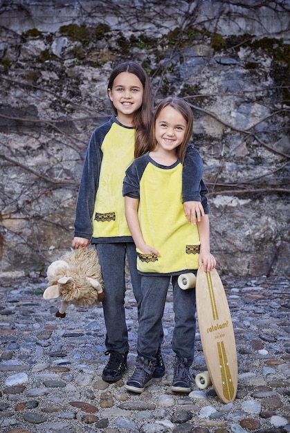 Duas fêmeas adolescentes bonitos com skate e brinquedo de pelúcia posando sobre fundo cinza natural.