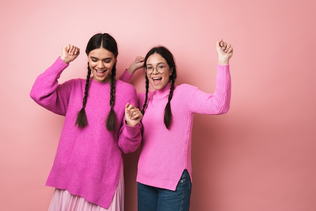 Duas garotas adolescentes alegres e fofas dançando isoladas sobre uma parede rosa, se divertindo