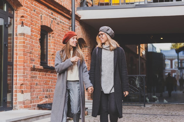 Duas garotas andando juntas na rua e segurando as mãos, elas estão usando primavera ou outono
