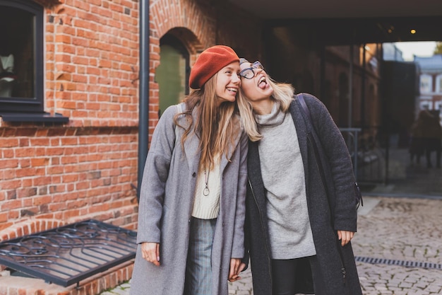 Duas garotas andando na rua juntas e de mãos dadas Elas estão vestindo roupas de primavera ou outono e estão felizes Amizade e conceito de relacionamento