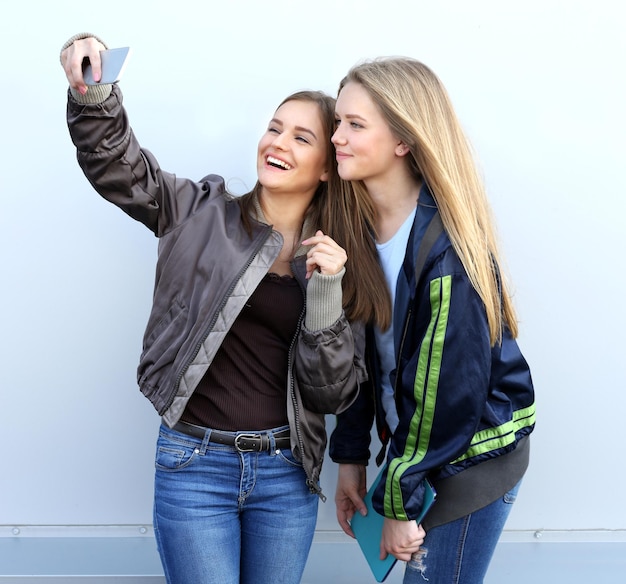 duas garotas andando pelas ruas rindo tirando fotos usando smartphone