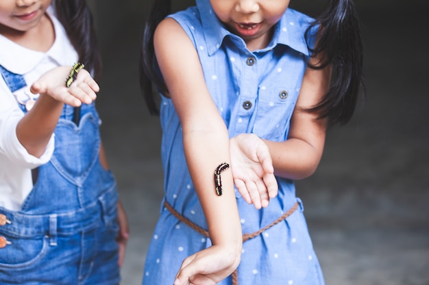 Duas garotas asiáticas bonito criança segurando e brincando com lagarta preta