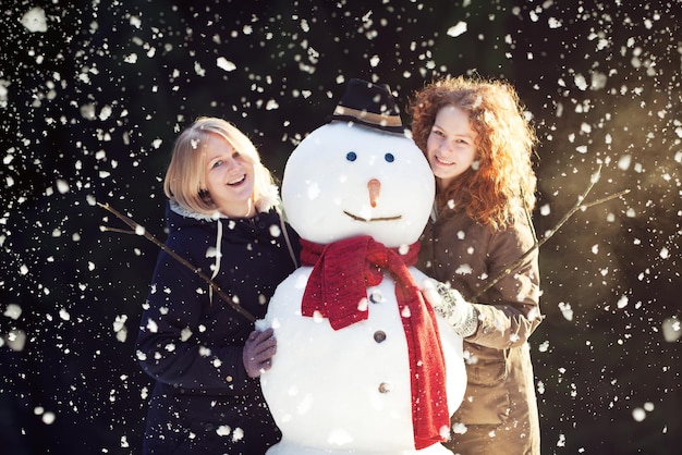 Duas garotas bonitas sorridentes posando com um boneco de neve em um parque