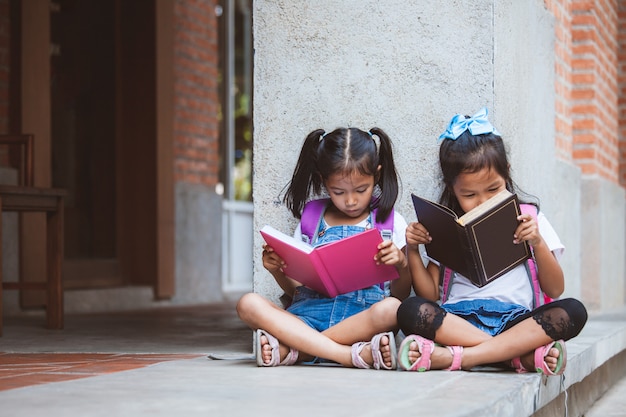 Duas garotas bonito aluno asiático lendo um livro juntos na escola com diversão e felicidade