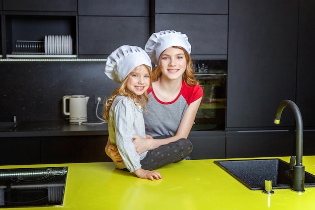 Duas garotas com chapéu de chef se abraçando e se divertindo na cozinha