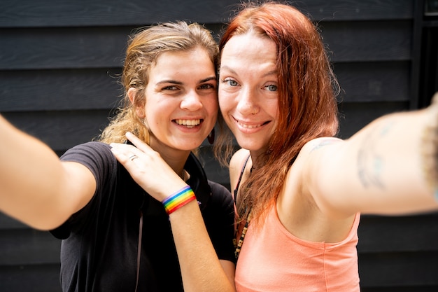 Duas garotas com uma pulseira com a bandeira lgtb fazendo uma selfie lá fora