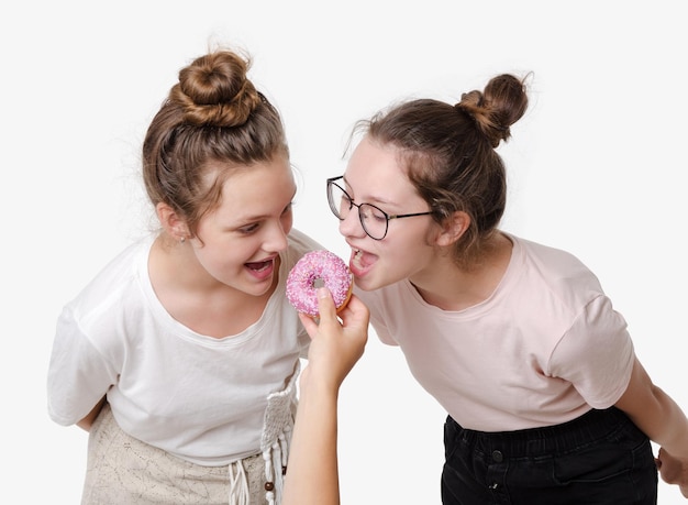 Duas garotas comem rosquinha doce e sorriem retrato de estúdio em fundo branco