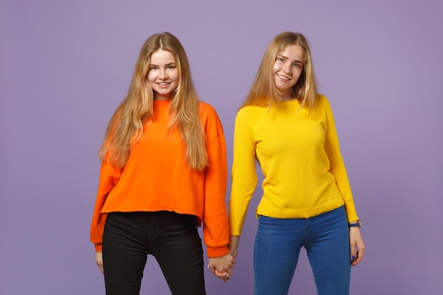 Duas garotas de irmãs gêmeas loiras jovens atraentes em roupas coloridas vivas isoladas na parede de azul violeta pastel. conceito de estilo de vida familiar de pessoas.