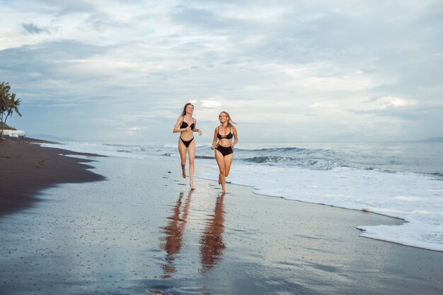 Duas garotas de maiô correndo na praia