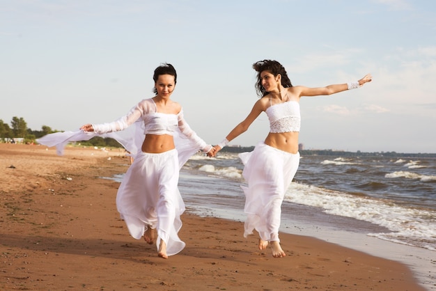 Duas garotas em vestido branco dançando na praia