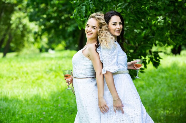 Duas garotas estão descansando no parque, sentadas em uma toalha de piquenique com frutas e vinho