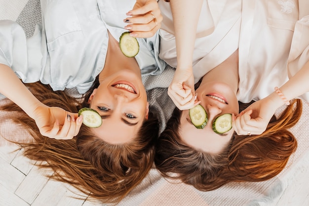 Duas garotas fazem máscaras caseiras de beleza para o rosto e os cabelos. pepinos para o frescor da pele ao redor dos olhos