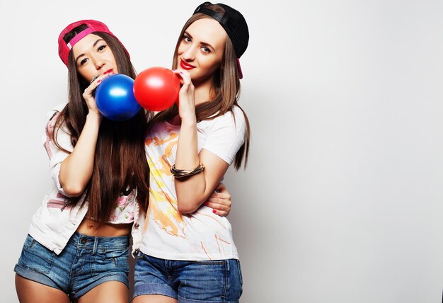 Duas garotas hipster felizes sorrindo e segurando balões coloridos sobre fundo branco