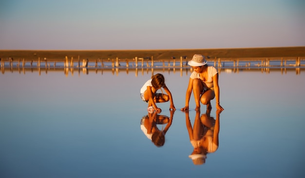 Duas garotas incrivelmente lindas em trajes incomuns em um lindo lago salgado transparente procuram algo em uma superfície brilhante