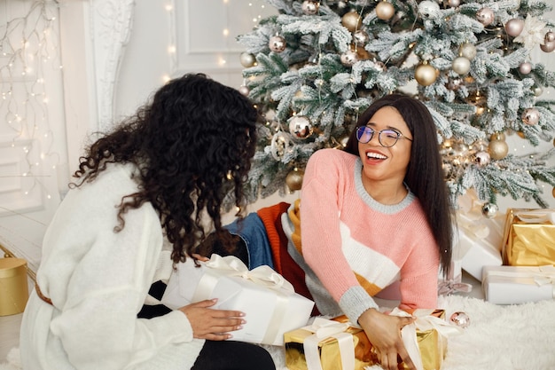 Duas garotas indianas em óculos sentados perto da árvore de Natal