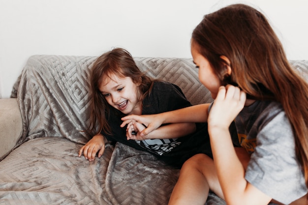 Duas garotas, irmãs brincando no sofá, abraços, risos, luta, camiseta