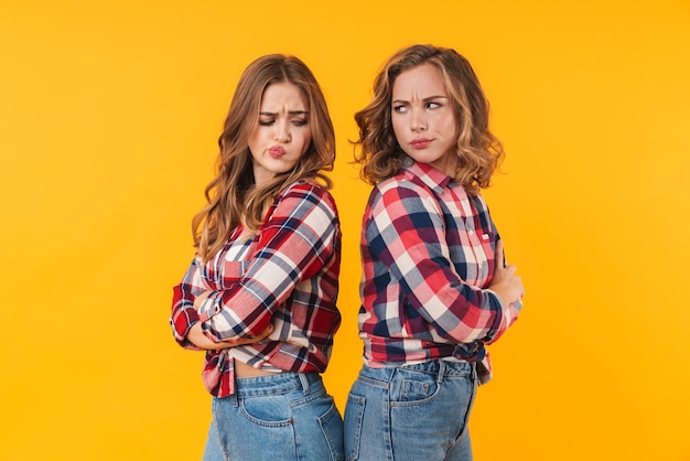 duas garotas lindas vestindo camisa xadrez franzindo a testa e isoladas costas com costas