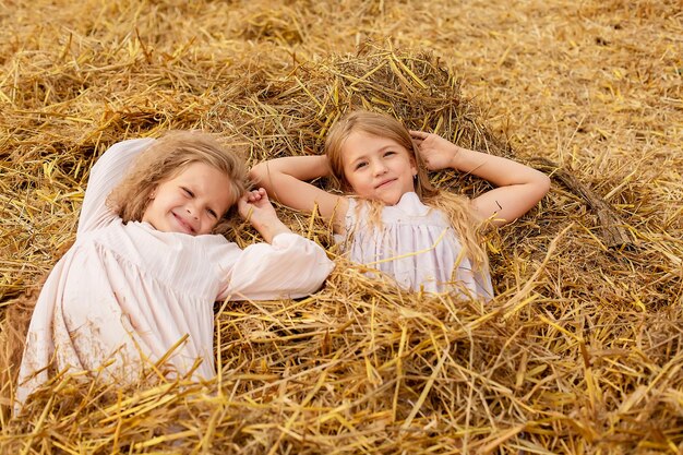 duas garotas loiras com cabelos longos em vestidos de linho estão em um palheiro em um campo ceifado
