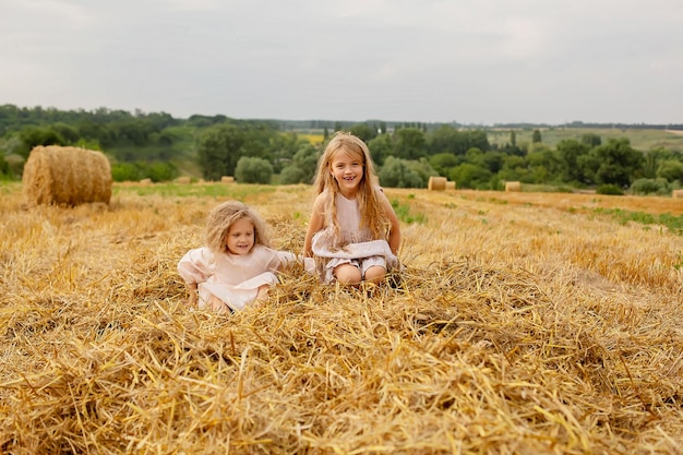 duas garotas loiras com cabelos longos em vestidos de linho estão em um palheiro em um campo ceifado