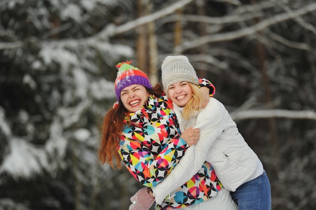 Duas garotas na floresta de inverno emocionalmente abraçam e sorriem. Mulheres felizes abraçam e expressam alegria.