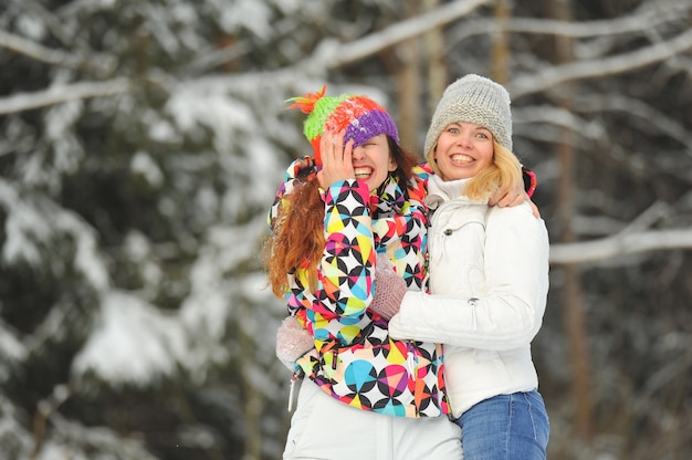 Duas garotas na floresta de inverno emocionalmente abraçam e sorriem. Mulheres felizes abraçam e expressam alegria.