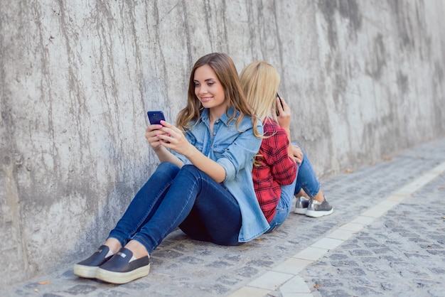 Duas garotas sentadas de costas e usando telefones celulares