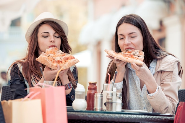 Duas garotas sorridentes comendo pizza no café