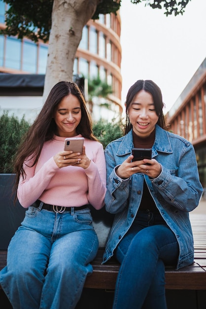 Foto duas garotas sorridentes usando seus smartphones enquanto esperam por seus amigos