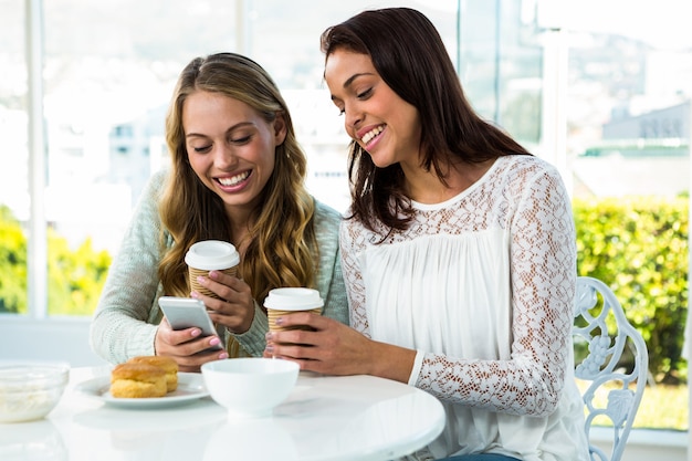 duas garotas usam um telefone enquanto comem e bebem
