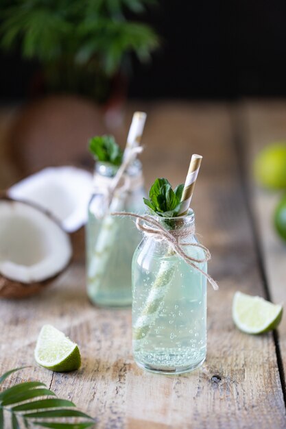 Foto duas garrafas de água de coco com hortelã e limão em uma mesa de madeira. bebida vegetariana. mojito. copie o espaço