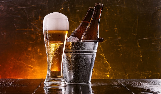 duas garrafas de cerveja em um balde com gelo e um copo de cerveja com espuma exuberante