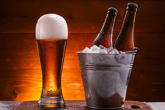 duas garrafas de cerveja em um balde com gelo e um copo de cerveja com espuma exuberante