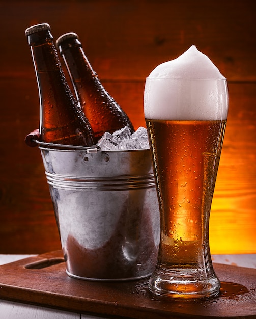 Duas garrafas de cerveja em um balde com gelo e um copo de cerveja com espuma exuberante