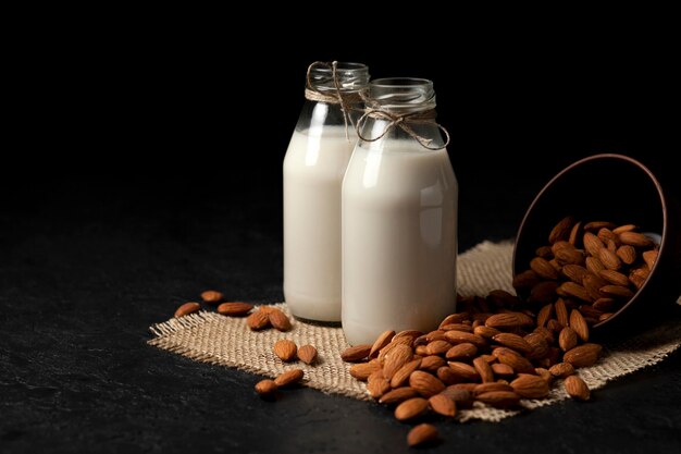 Duas garrafas de leite de amêndoa com nozes em uma mesa preta escura leite vegetariano sem açúcar e lactose
