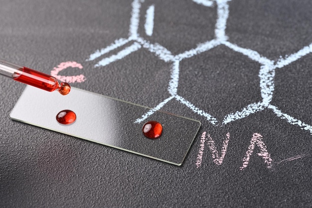 Duas gotas de líquido vermelho na lâmina do microscópio e fórmula química no fundo