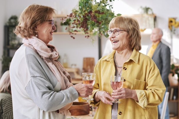 Duas idosas sorridentes conversando e bebendo vinho tinto na reunião