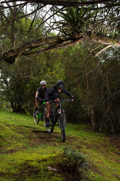 Duas intrépidas ciclistas descendo uma montanha no meio das árvores montadas em suas bicicletas