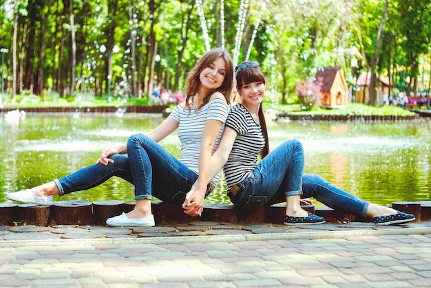 Duas irmãs, amigas se divertem, riem, comem algodão doce, caminham em um parque de diversões verde de verão. Feliz