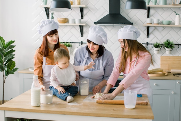 Duas irmãs, avó e filha bebê cozinhar torta de férias na cozinha para o dia das mães, série de fotos de estilo de vida casual no interior da vida real