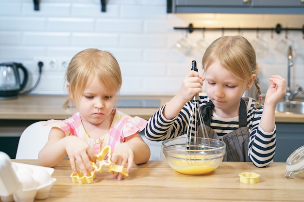 Duas irmãs bonitos preparando massa de biscoito. Meninas, ajudando a mãe na cozinha